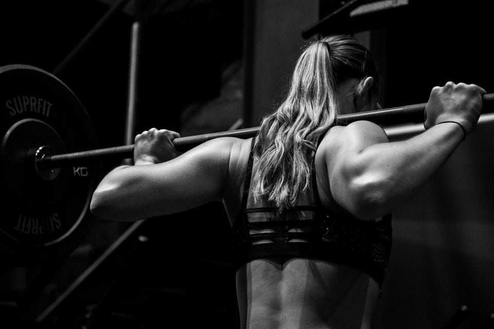 Fitness girl lifting weights in gym with barbell on her back.